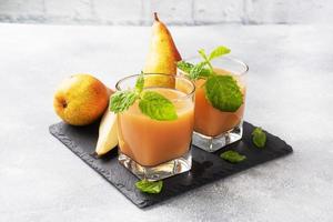 Natural pear juice in a glass cup. Juicy ripe conferences pears and mint leaves. copy space Slate stand, light concrete background. photo