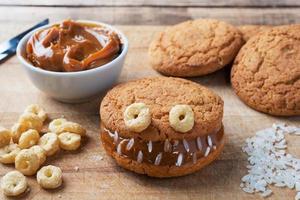 Cookies with cream paste in the shape of monsters for Halloween celebration. Funny homemade faces made of oatmeal cookies and boiled condensed milk.