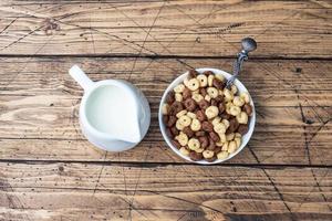 cereales secos para el desayuno. anillos de chocolate y maíz hechos de cereales naturales con leche en un plato. fondo rústico de madera, espacio de copia. foto