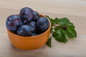 ciruelas frescas en un recipiente sobre fondo de madera foto