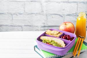 Delicious healthy sandwich in a lunch box, cookies and cherries. Take lunch with you to school or the office. Juice in a bottle and an apple. photo