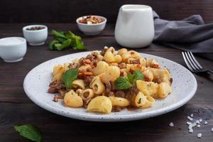 Stewed pasta with minced beef and vegetables, macaroni in Navy style on a plate. Dark wooden background. photo