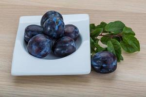 Fresh plums in a bowl on wooden background photo