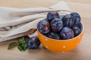 Ripe fresh plum in a bowl on wooden background photo