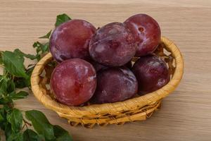 Fresh plums in a basket on wooden background photo
