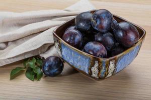 Ripe fresh plum in a bowl on wooden background photo