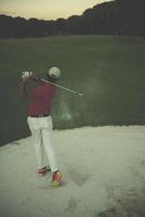 golfer hitting a sand bunker shot on sunset photo