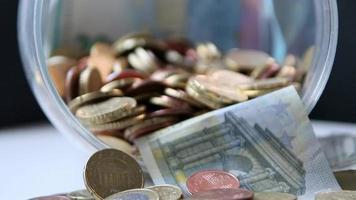 Euro-Geld-Einsparungen, die in ein Glasgefäß voller Euro-Münzen und Euro-Banknoten gleiten, für die Finanzverwaltung von Taschengeld und Trinkgeld oder Trinkgeld für Sparschwein-Währungsstapel als Bargeld-Nahaufnahme-Makroansicht