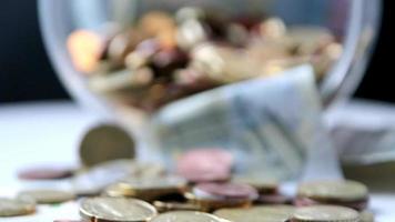 Euro money savings sliding inside glass jar full of Euro coins and Euro banknotes for financial management of pocket money and tip or gratuity for piggy bank currency pile as cash close-up macro view video