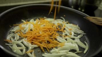 pedaços de cebola e cenoura fatiados fritos em uma panela de close-up. fritar cebola e cenoura em óleo de girassol em uma panela quente video