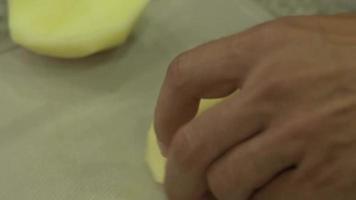la mano corta las patatas de cerca. manos cortando patatas en una tabla de cortar de madera. cortar verduras con un cuchillo para cocinar. metraje de vídeo video