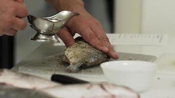 mãos masculinas preparam vários peixes para assar em uma assadeira. adicione óleo, sal e especiarias ao peixe. processo de cozimento. video