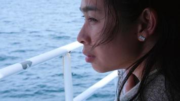 retrato de uma mulher asiática, observando a vista em uma balsa navegando no mar. Feche o rosto da mulher com belas paisagens marinhas vista do iate. video