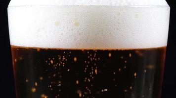 Close-up Of Glass Of Beer. This stock footage features a close-up shot of a rotating glass of beer. It shows some bubbles rising and forming a layer of thick white foam at the top. video