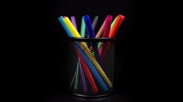 Colored pens in pencil case rotating in the isolated dark ,black background.