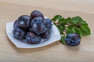 Fresh plums on the plate and wooden background photo