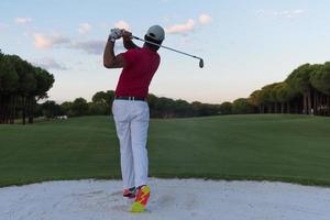 golfer hitting a sand bunker shot on sunset photo