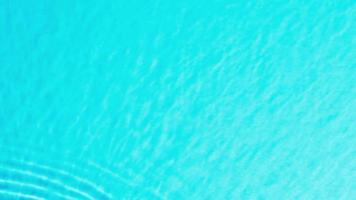 topp se långsam rörelse av släppa falls in i vatten och divergerande cirklar av vatten på blå bakgrund. Sol och skuggor. vatten släppa stänk på de yta av de vatten. kosmetisk för design reklam video