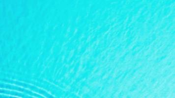 Top view slow motion of drop falls into water and diverging circles of water on blue background. Sun and shadows. Water drop splash on the surface of the water. cosmetic for design advertising video