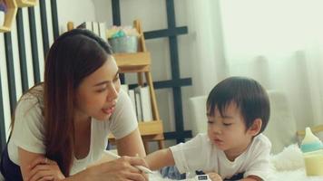 mãe asiática e filho brincando alegremente na cama juntos. mãe ensina lição de casa e ensina as crianças a desenhar. video