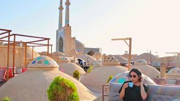 Yazd, Iran, 2022 - female caucasian person drink persian coffee in traditional rooftop cafe relax enjoy panoramic views of old town video