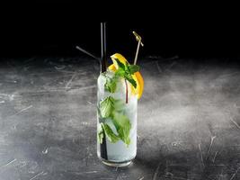 Cold alcoholic or non-alcoholic cocktail f the Mojito type with ice on dark background photo