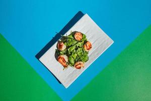 Salad with shrimps and arugula on white dish on colored background photo