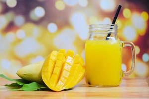 jugo de mango de verano en frasco de vidrio con dulce rebanada madura de mango en hojas verdes de árboles de frutas tropicales foto