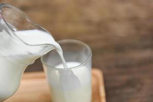 Fresh milk natural in a glass jug and  Pouring milk into glass on wooden background - photo