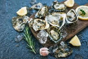 ostras frescas mariscos en el fondo de la placa de madera - concha de ostra abierta con hierbas especias limón romero servido mesa y hielo marisco saludable cena de ostras crudas en el restaurante comida gourmet foto