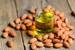 aceite de almendras y nueces de almendras en madera, delicioso aceite de almendras dulces en vidrio, nueces de almendras tostadas para alimentos saludables y aceites vegetales orgánicos para meriendas para cocinar o spa foto