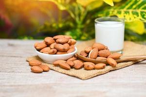 Almond milk and Almonds nuts on white bowl with green leaf on sack background, Delicious sweet almonds on the wooden table , roasted almond nut for healthy food and snack photo