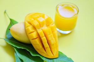 Mango summer juice in glass with sweet ripe slice of mango on green leaves from tree tropical fruit photo