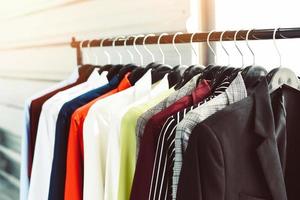 ropa de moda para hombres: ropa colgada, traje colorido o estante de armario, trajes de hombre de diferentes colores en un armario en perchas en una tienda o sala de exposición foto