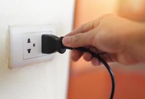 Plug in wall with hand and black power cord cable - Unplug or plugged in concept socket on electric plug on wall photo