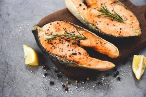 Grilled salmon steak with herbs and spices rosemary lemon on wooden cutting board background - Close up cooked salmon fish fillet steak seafood photo