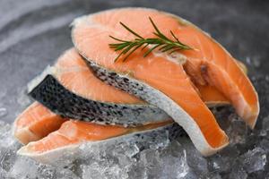 Fresh raw salmon steak with herbs rosemary on black plate background - Close up of raw salmon fish fillet and ice photo