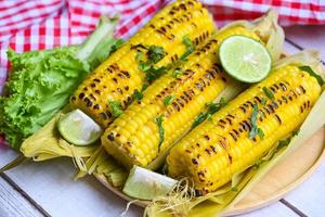 mazorcas de maíz maduras maíz dulce a la parrilla para comida vegana cena o merienda, comida de maíz dulce con limón y cilantro, maíz dulce cocinado sobre fondo de madera foto