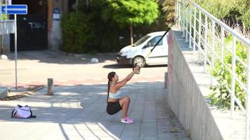 Fit young woman exercises in public space using suspension bands video