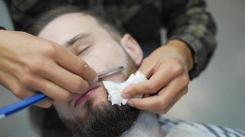 Barber shaves man's face and shapes beard with straight razor video
