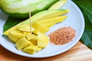 Rebanada de mango en plato blanco y hojas del concepto de fruta de verano tropical de árbol - mango maduro en escabeche y mangos verdes para la merienda foto