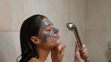 mujer joven enjuaga la máscara de arcilla de la cara en la ducha video