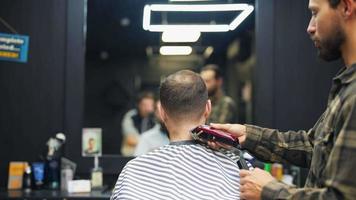 coiffeur coupe l'arrière de la tête des cheveux et du cou du client masculin avec un peigne et une tondeuse video