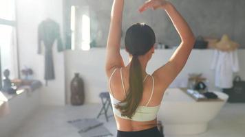 Mettre en place une jeune femme dans les danses de vêtements actifs de loisirs renversant les cheveux dans une salle de bains ensoleillée video