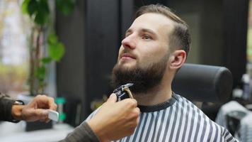 Barber trims face and neck hair of male client with comb and clippers video