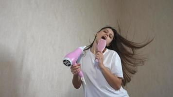 Woman blow drying hair jumps up and down dancing singing into pink hair brush in slow motion video