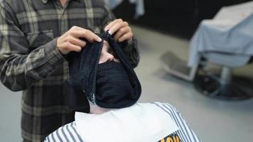 Barber wraps client's face with warm towel and while talking video