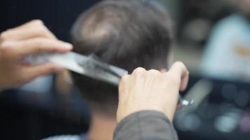 Barber trims back of head hair with comb and thinning shear scissors