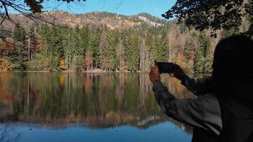 Nahaufnahme einer kaukasischen Frau, die am See steht und ein Panoramafoto der malerischen Herbstnatur im Freien macht