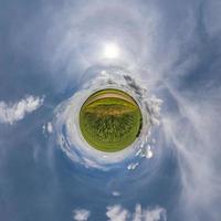 green tiny planet in blue sky with beautiful clouds. Transformation of spherical panorama 360 degrees. Spherical abstract aerial view. Curvature of space. photo